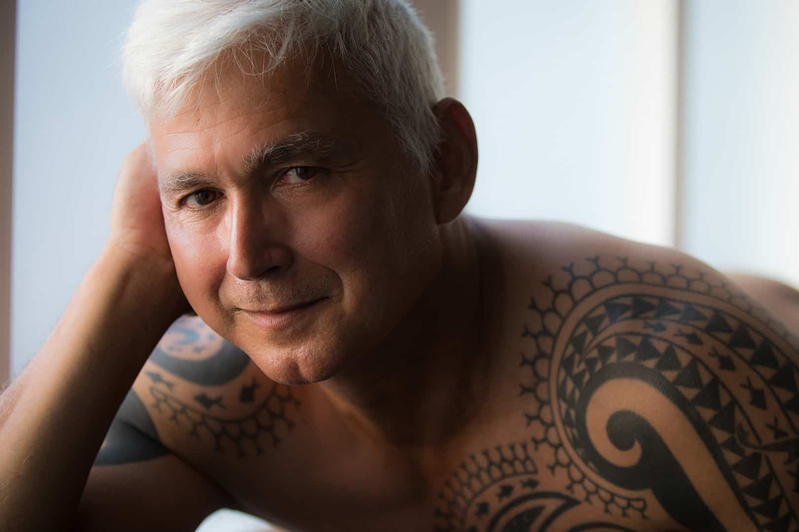boudoir image of tattooed man smiling at the camera