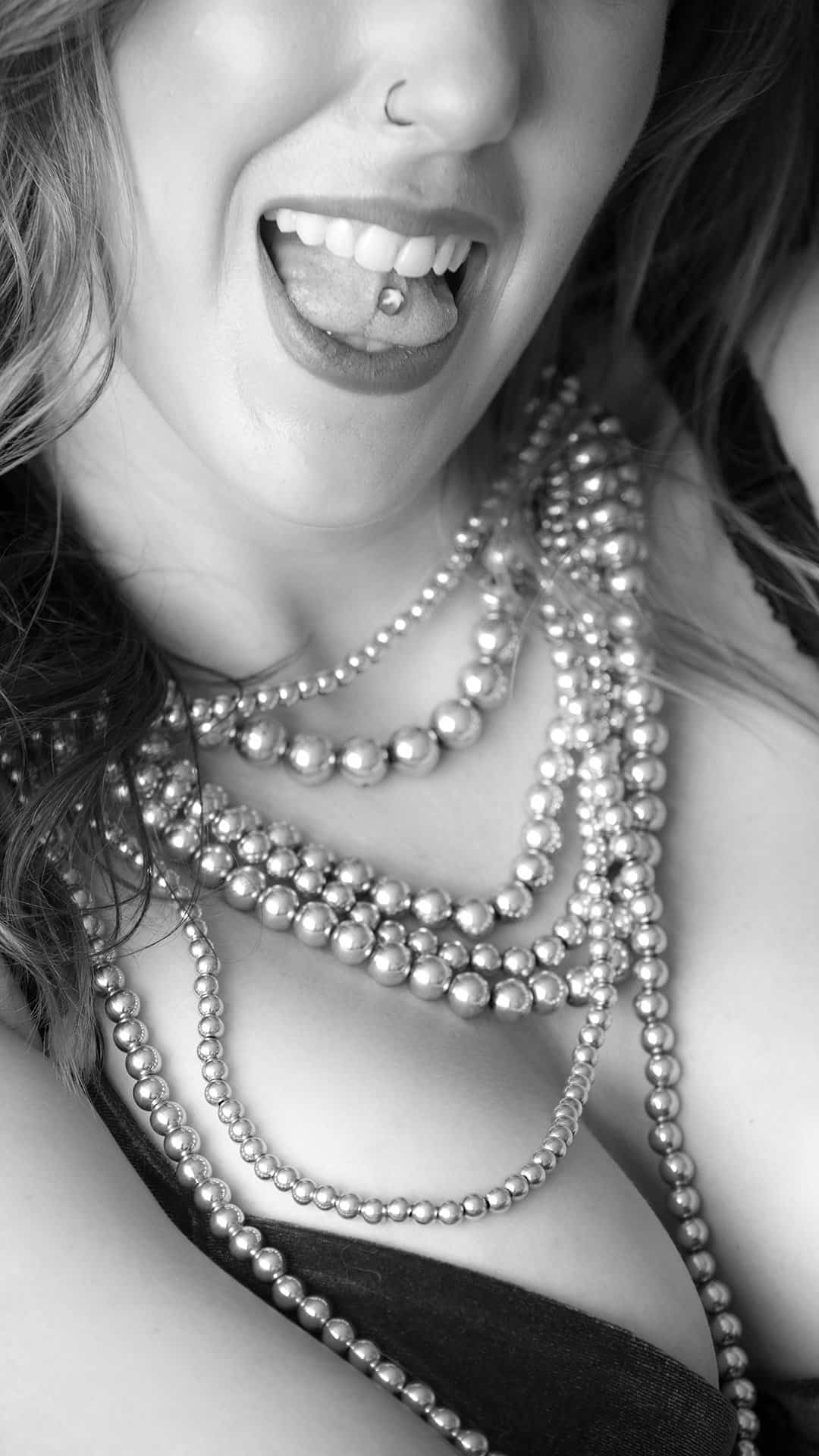 boudoir image of woman draped in pearls, showing off a tongue stud