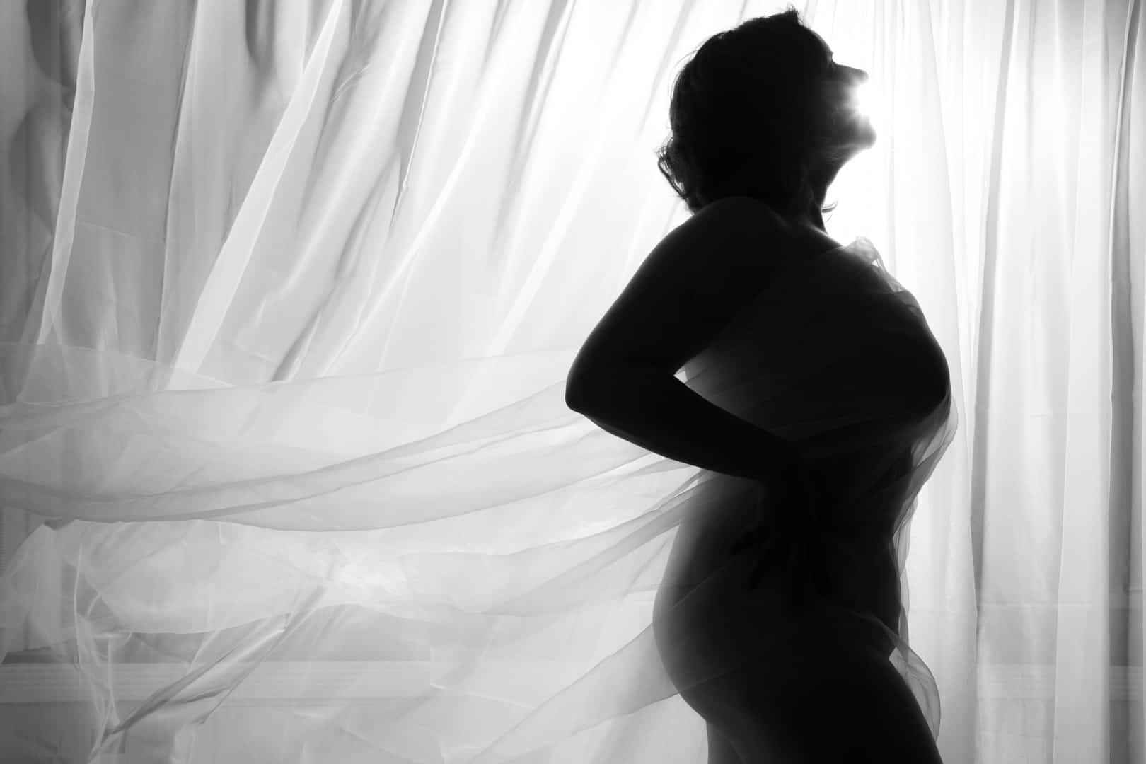  boudoir image of woman in silhouette against sheer curtains