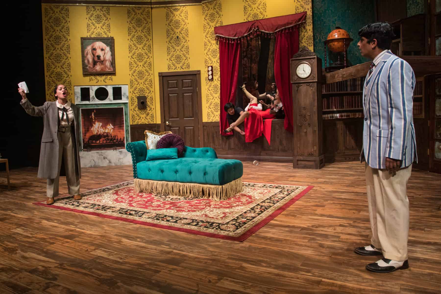 Production photo from "The Play That Goes Wrong" at Valley Christian Schools: a dramatic moment with characters staring each other down while a woman is pulled tumbling through a window